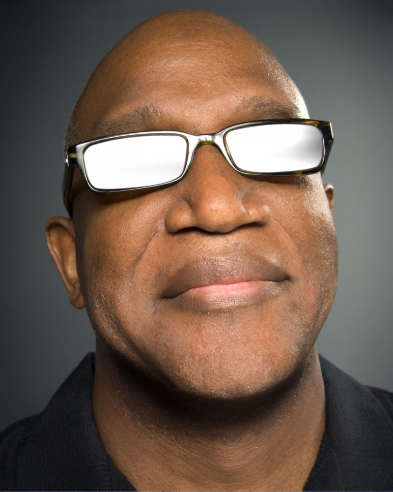 Close-up vertical headshot of male, pianist and keyboardist, musician, with reflective shades on.