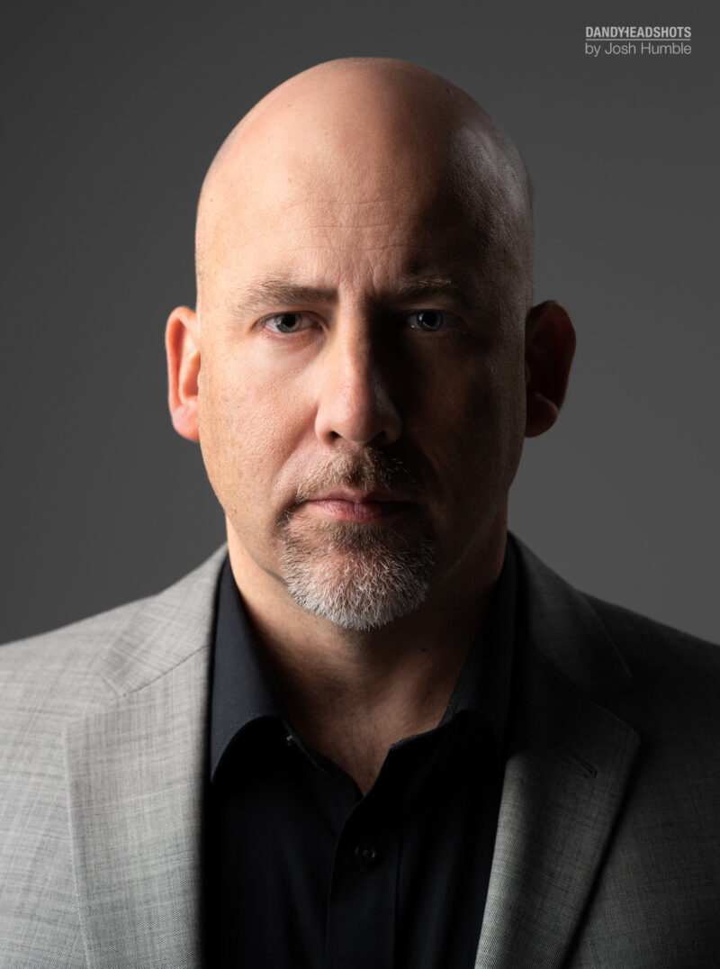 Actor headshot, male subject, low-key with split lighting.