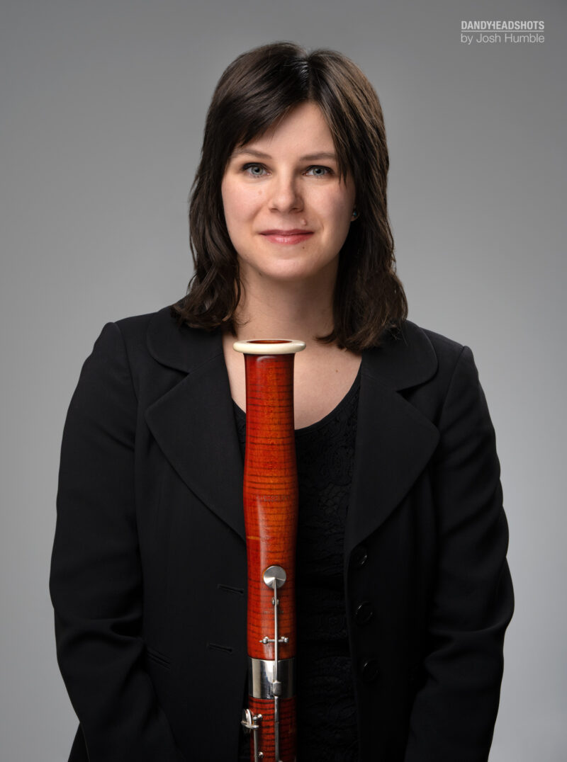 Female bassoonist holding bassoon with black backdrop.